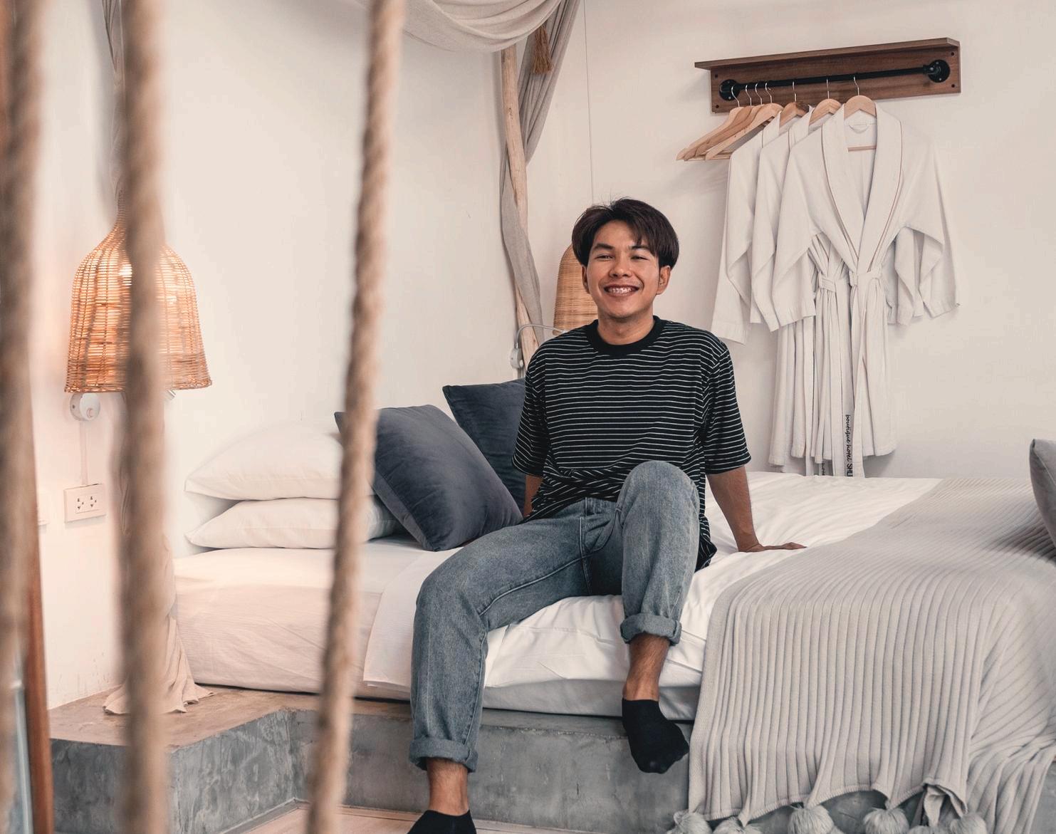 A smiling guest sitting on the bed among woven lights and natural wood details